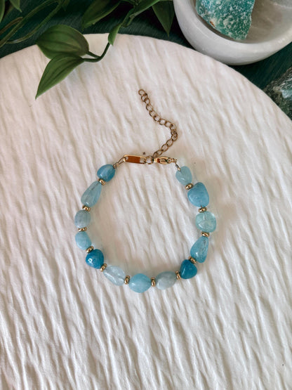 Goldenes Aquamarin Perlenarmband mit blauen Natursteinen liegend auf weißem Tablett, Sicht von oben