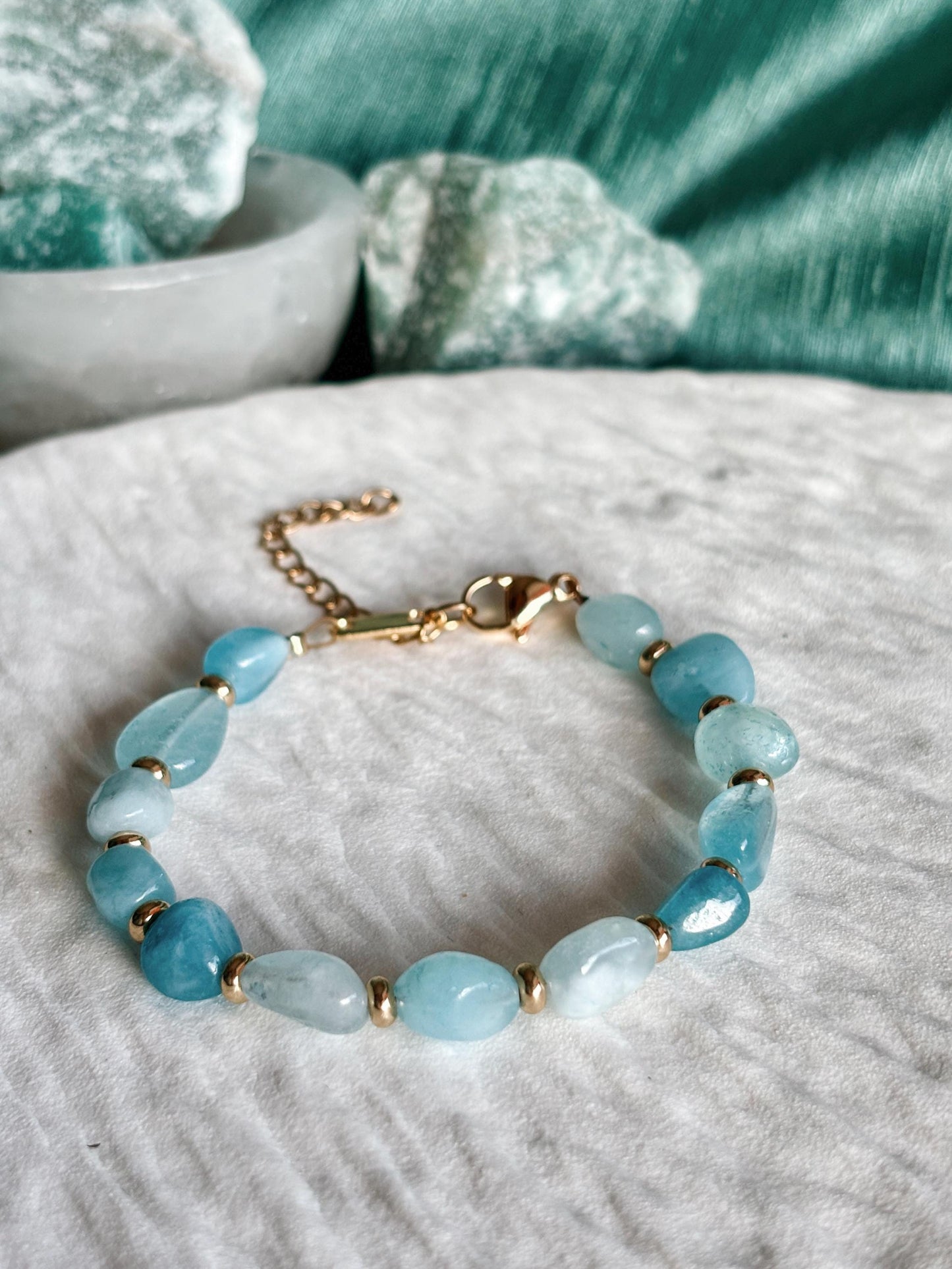 Goldenes Aquamarin Perlenarmband mit blauen Natursteinen liegend auf weißem Tablett, Detailaufnahme