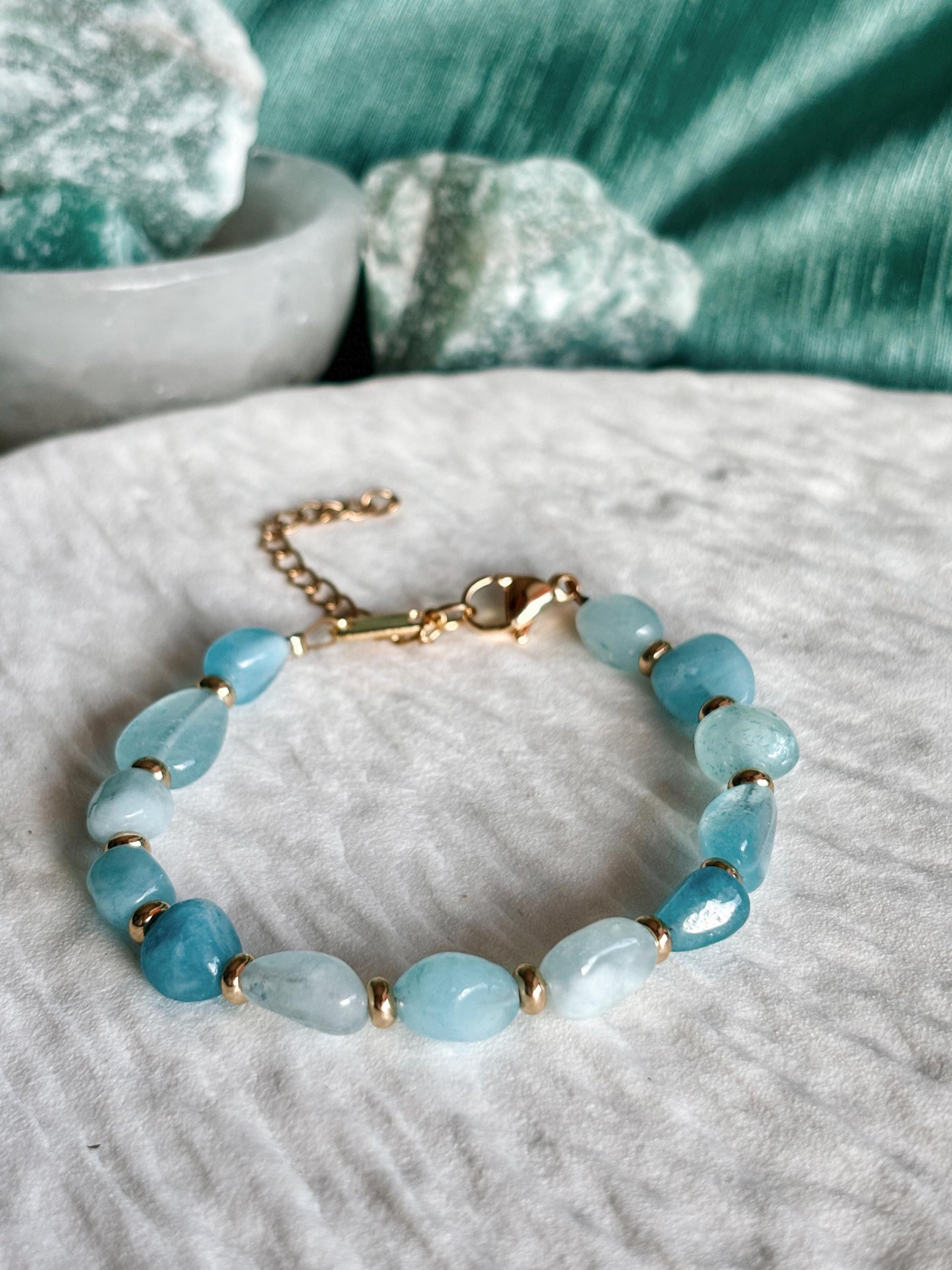 Goldenes Aquamarin Perlenarmband mit blauen Natursteinen liegend auf weißem Tablett, Detailaufnahme