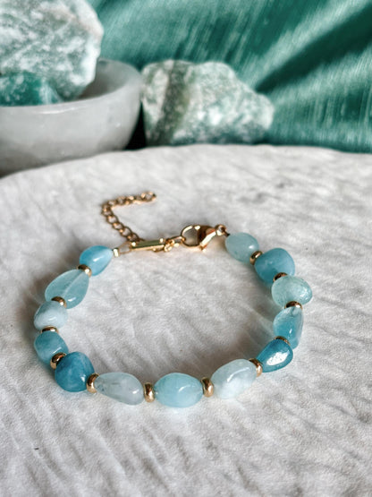 Goldenes Aquamarin Perlenarmband mit blauen Natursteinen liegend auf weißem Tablett, Detailaufnahme