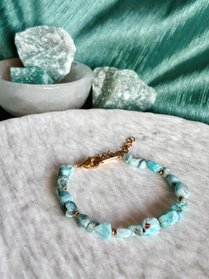 Goldenes Larimar Perlenarmband mit blauen Natursteinen liegend auf weißem Tablett, Detailaufnahme