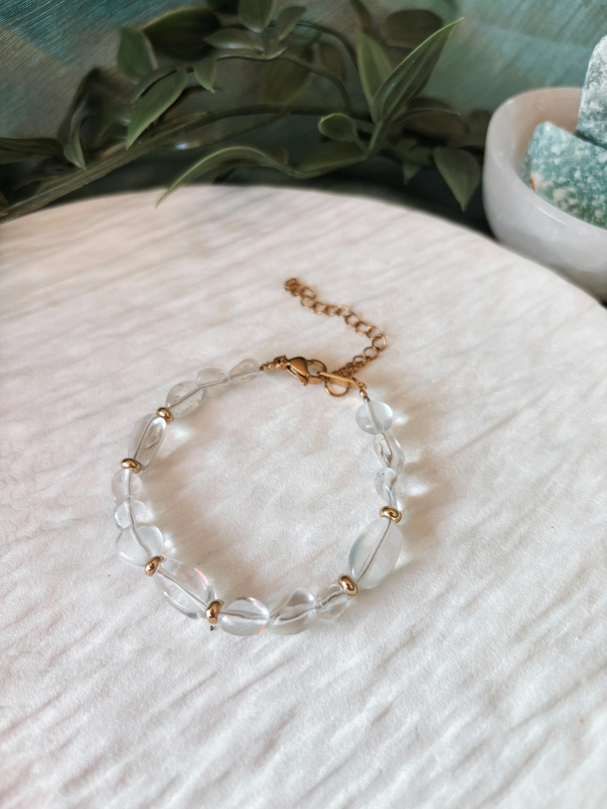 Goldenes Bergkristall Perlenarmband mit transparenten Natursteinen liegend auf weißem Tablett, Ansicht von oben