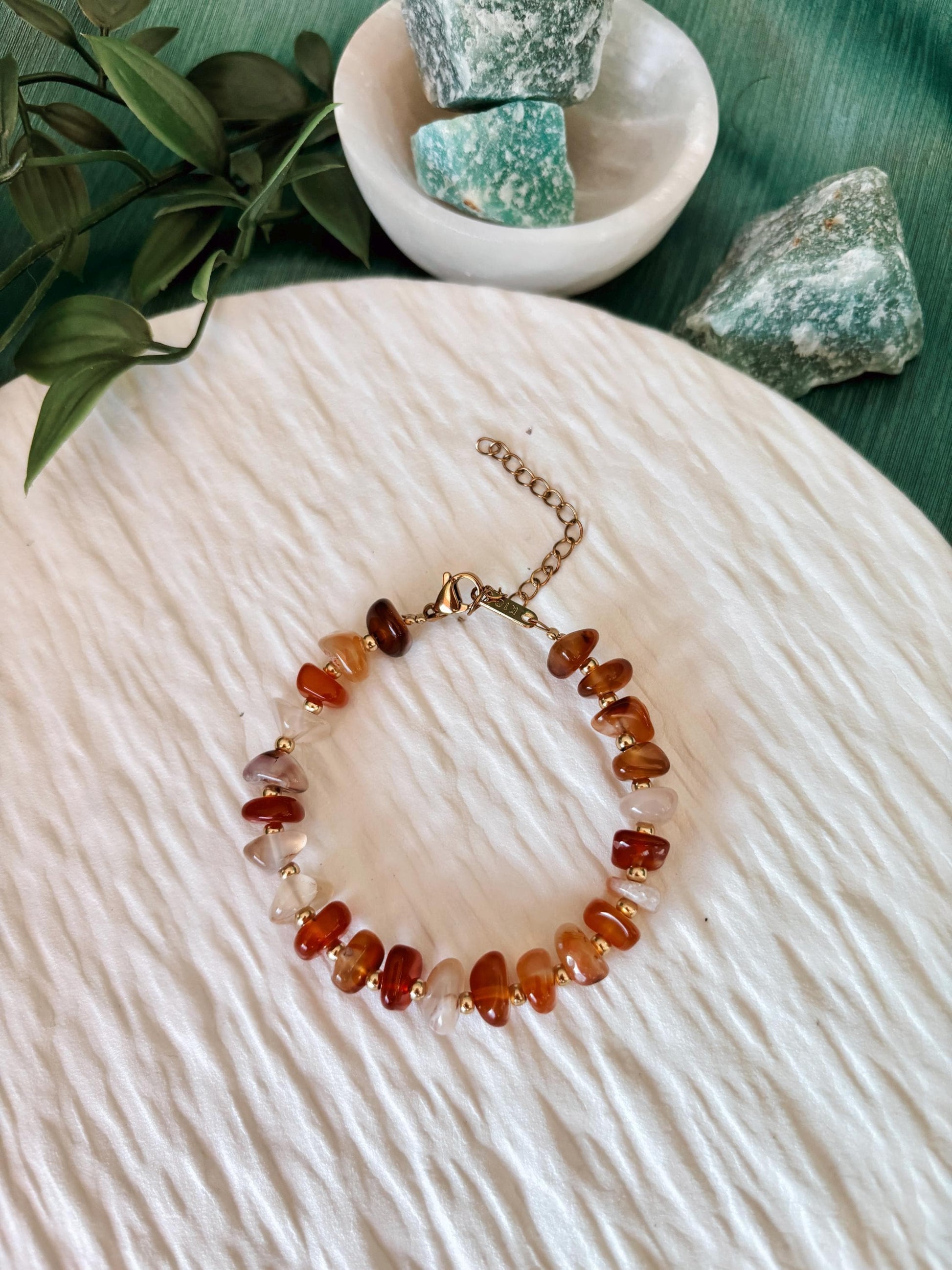 Goldenes Karneol Perlenarmband mit roten Natursteinen liegend auf weißem Tablett, Ansicht von oben
