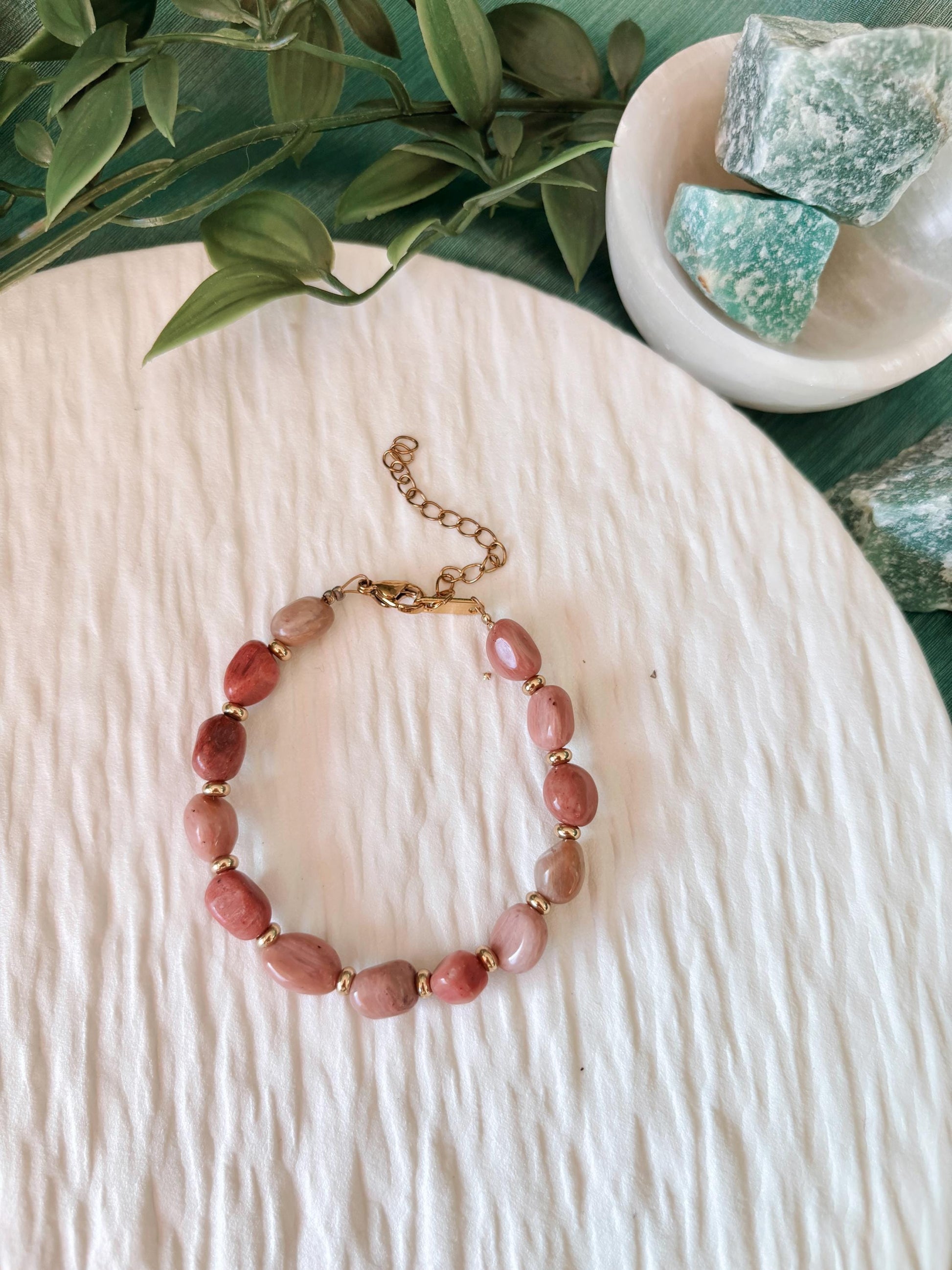 Goldenes Rhodonit Perlenarmband mit rosa Natursteinen liegend auf weißem Tablett, Ansicht von oben