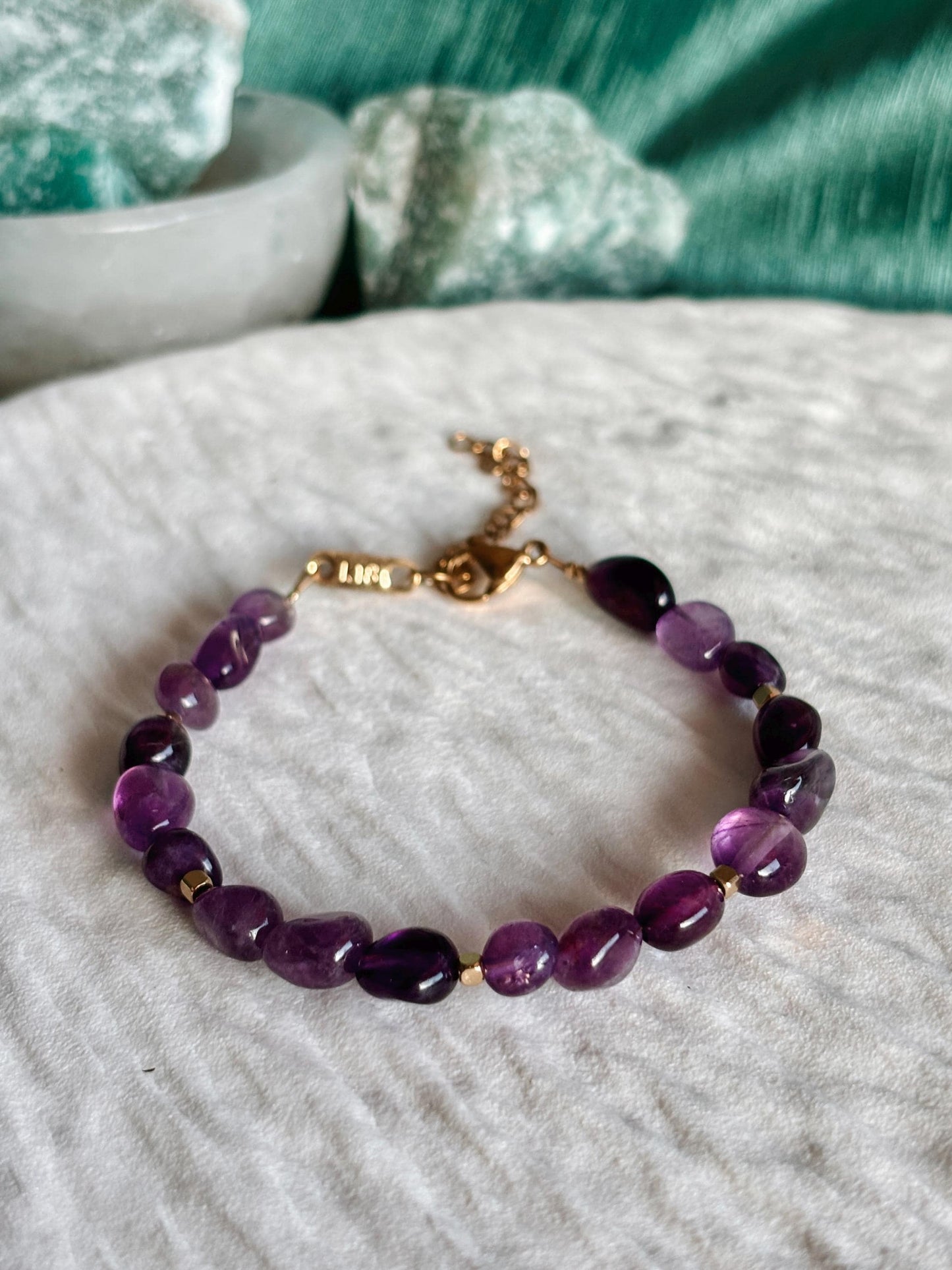 Goldenes Amethyst Perlenarmband mit lila Natursteinen liegend auf weißem Tablett, Detailaufnahme