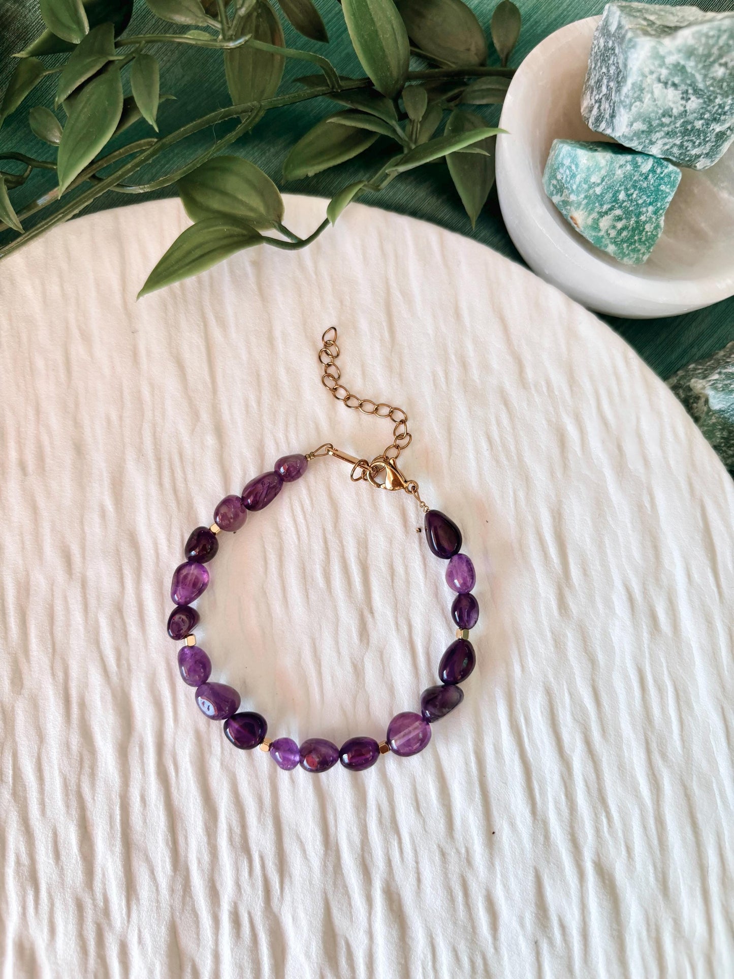 Goldenes Amethyst Perlenarmband mit lila Natursteinen liegend auf weißem Tablett, Ansicht von oben