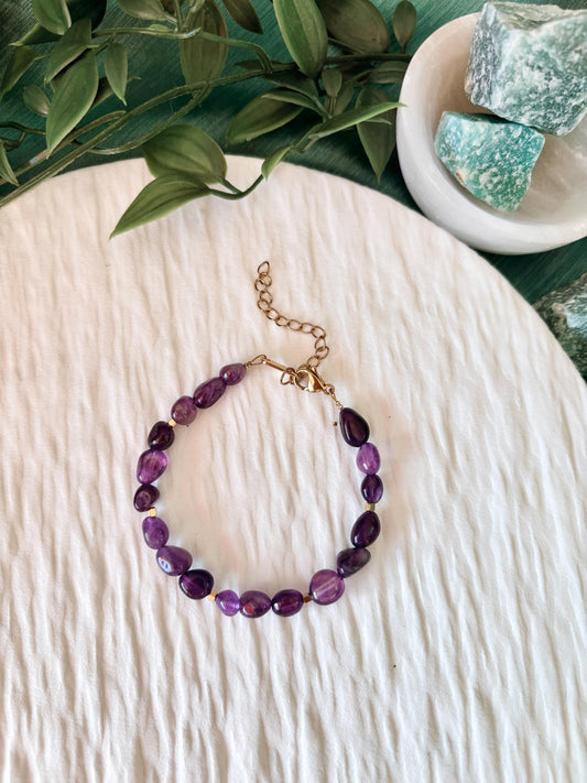 Goldenes Amethyst Perlenarmband mit lila Natursteinen liegend auf weißem Tablett, Ansicht von oben