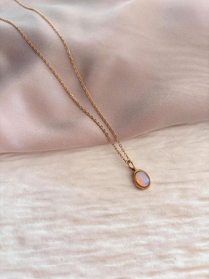 Kette mit opalisierendem Anhänger vor einem sanften, rosa Stoffhintergrund.