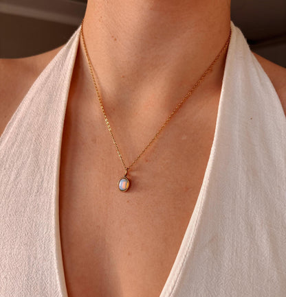 Goldkette mit Opal-Anhänger, getragen von einer Person mit weißem Oberteil.