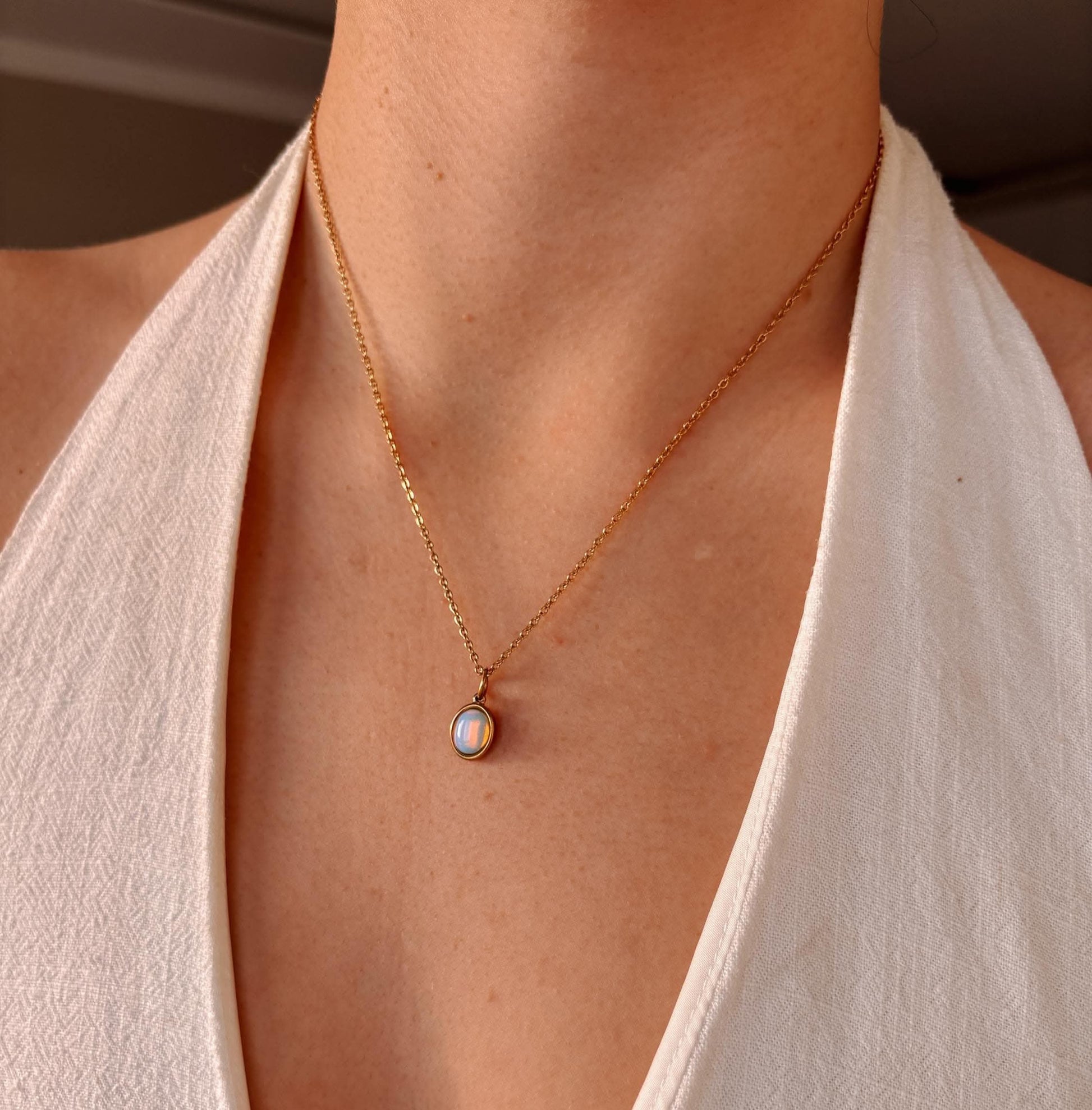 Frau trägt eine goldene Opalkette mit ovalem Anhänger auf hellem Top.