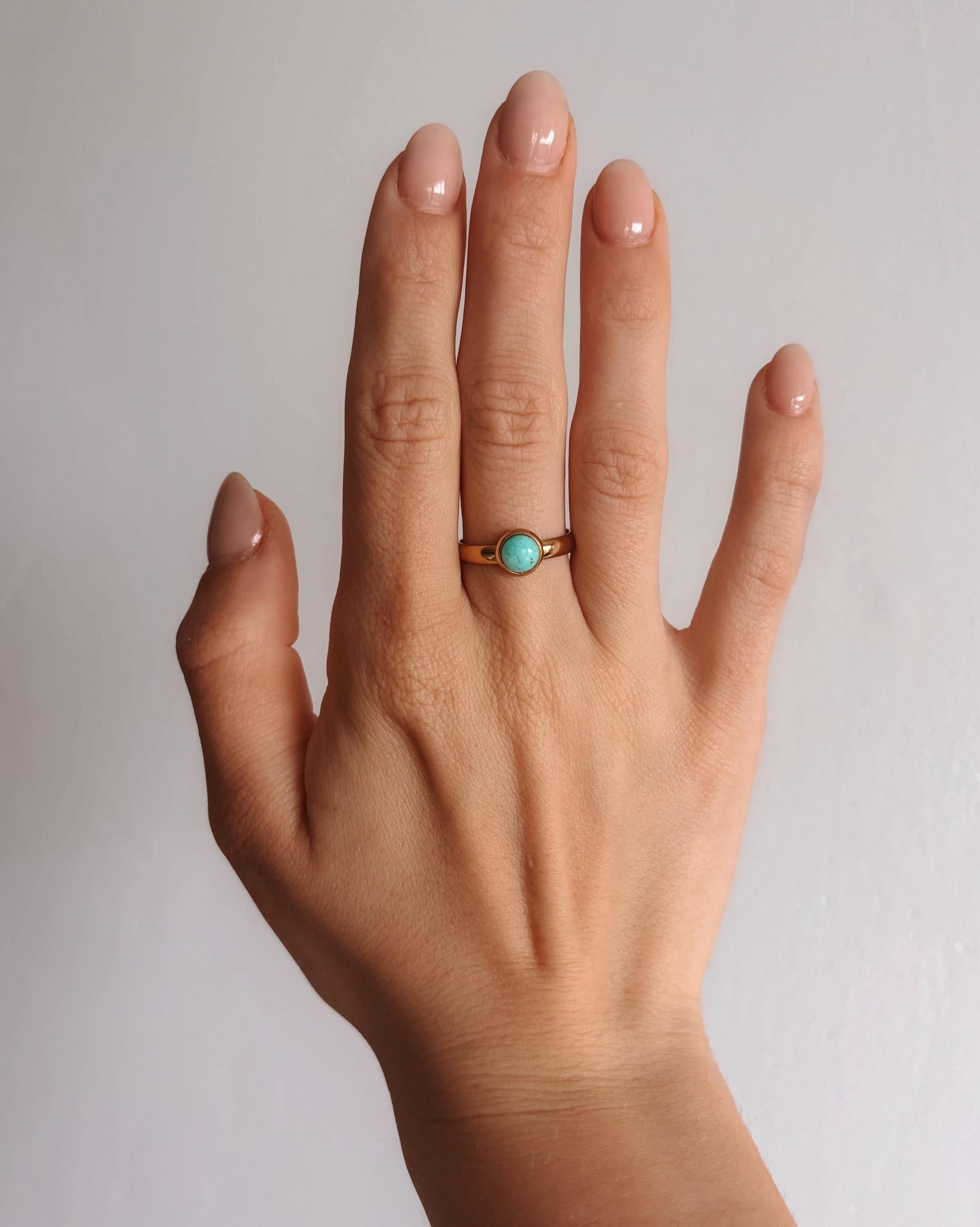 Hand mit amazonit-ring-amaya auf dem Ringfinger, schlichter Goldring mit einem türkisfarbenen Stein.