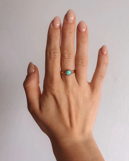 Hand mit amazonit-ring-amaya auf dem Ringfinger, schlichter Goldring mit einem türkisfarbenen Stein.