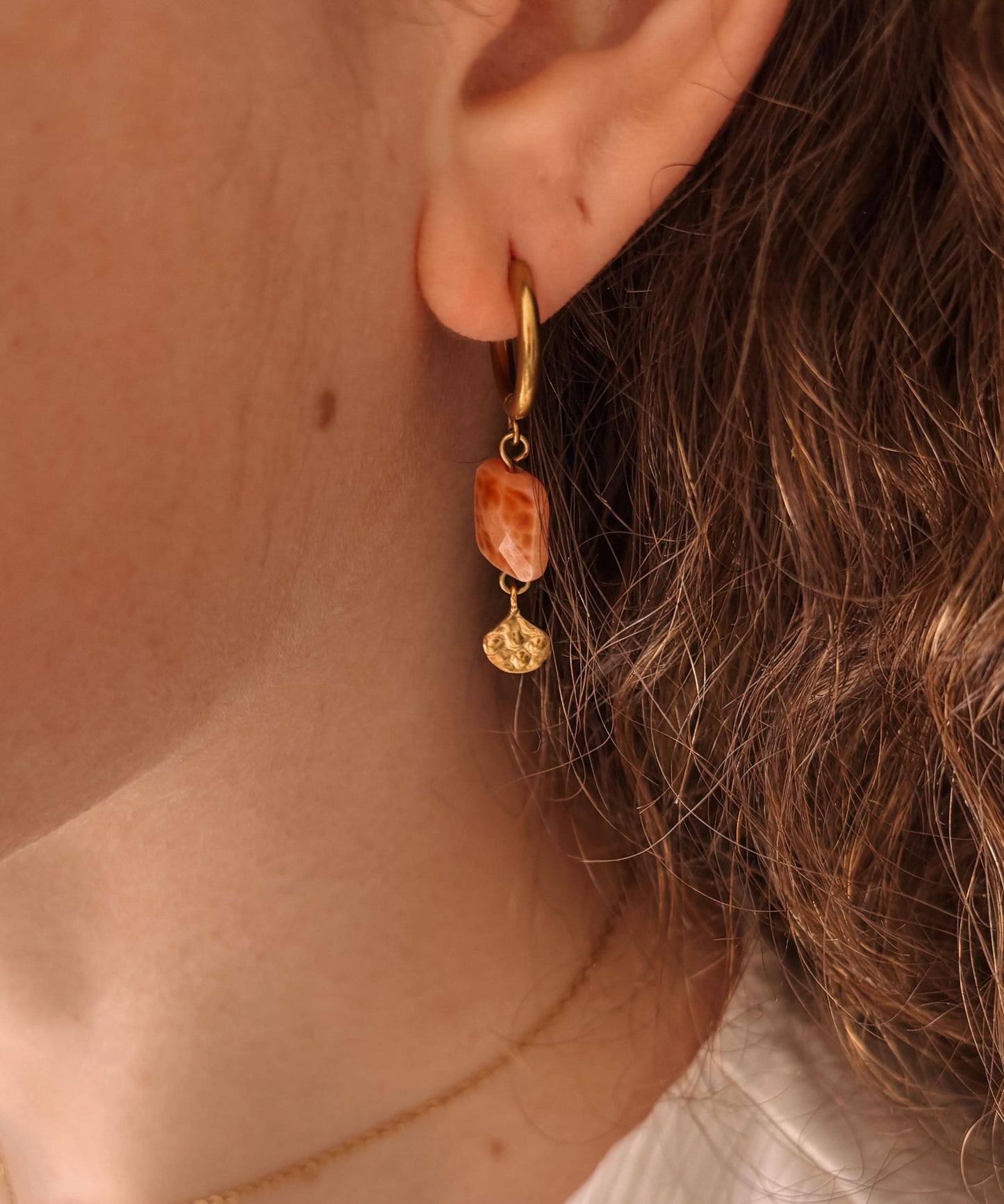 Goldener Creolen-Ohrring mit Achat-Anhänger "Moana" an einem Ohr, hervorgehobene Details und dezente Locken.