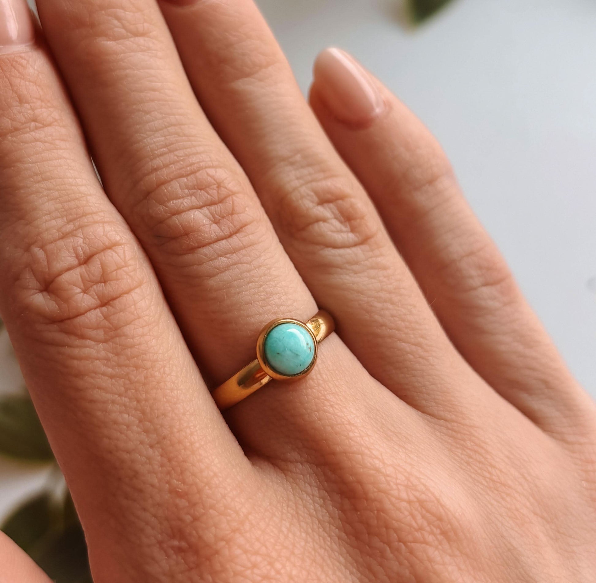 Hand mit einem goldenen Ring, der einen runden Amazonit-Stein zeigt, getragen an einem Finger.